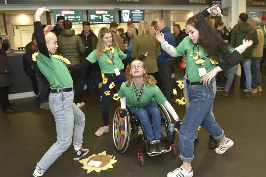 images of young dancers performing in green t-shirts and sunflower wreaths around their necks, during half time at a very busy rugby game